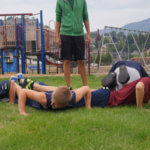 teen males do pushups by a playground