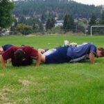 teen males do push ups in a field