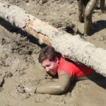 mud covered teen climbing under log