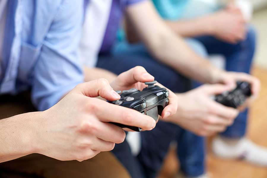 two pairs of hands hold gaming controllers while clasped hands in background reflect someone giving the gaming addiction self test