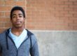 a teen leans against a brick wall and smiles because he's saying bye bye boot camp