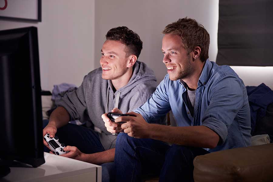 two male teens laugh and play video games before getting a gaming addiction diagnosis