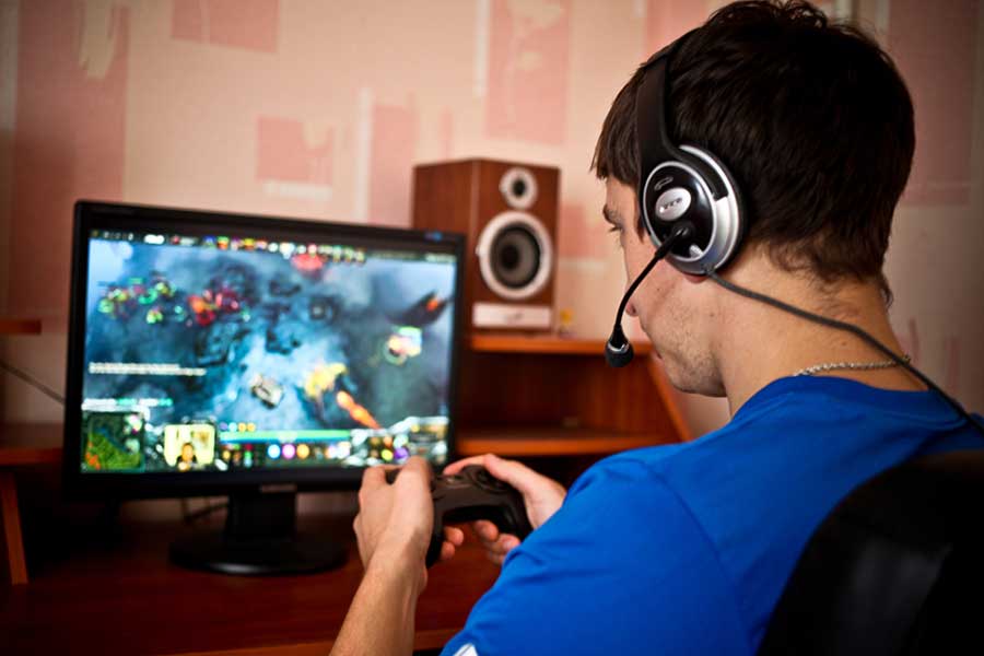 a male at a computer with headset on intensely plays video games displaying the top ten signs of gaming addiction