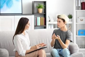 Young man sitting on couch with therapist during addiction counselling