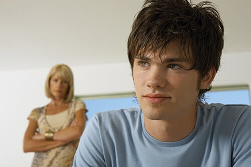 a teen boy sits while his mother looks at him with crossed arms and asks am i overreacting