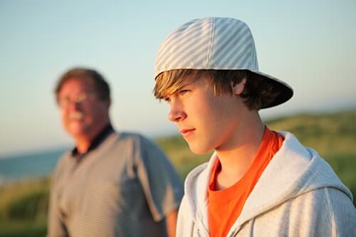 boy with backwards hat looks into the distance with concerned father debating sending his child away