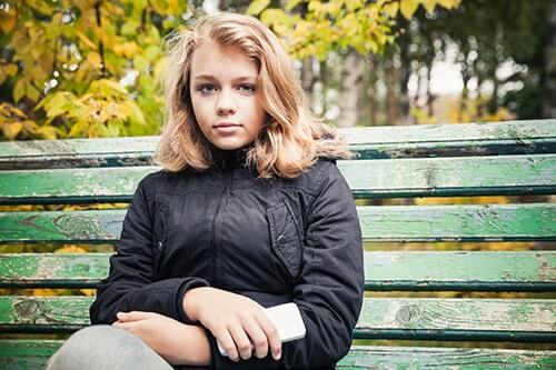 young teen sits on park bench being a resistant teen