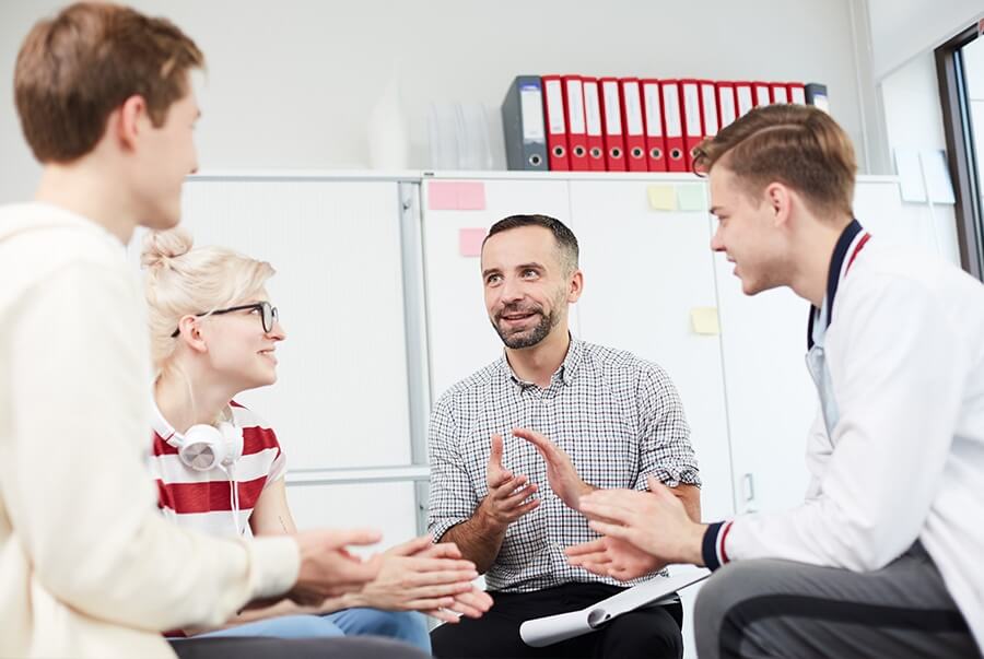 a counselor sits in a circle with two male teens and a female teen having a discussion