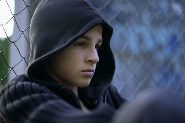 troubled teen in hoodie sitting against chain fence