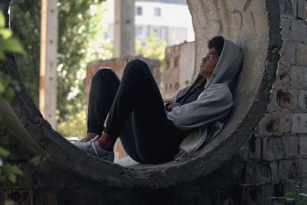a teen sits alone in building ruins presumably under the influence of a substance or drug and in need of treatment