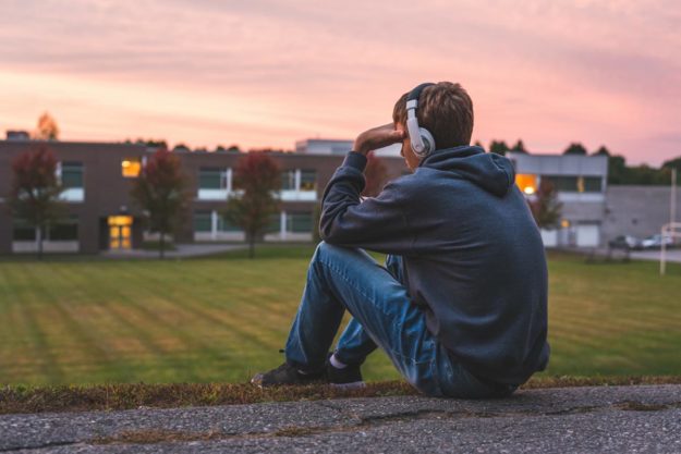 a teen boy sits on the ground outside near a football field and trying to figure out what it means to be helping teens with depression