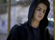 a delinquent teen with his hood up stands against a fence